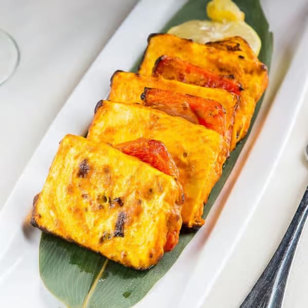 Grilled paneer tikka skewers with bell peppers, served on a banana leaf with lemon wedges.