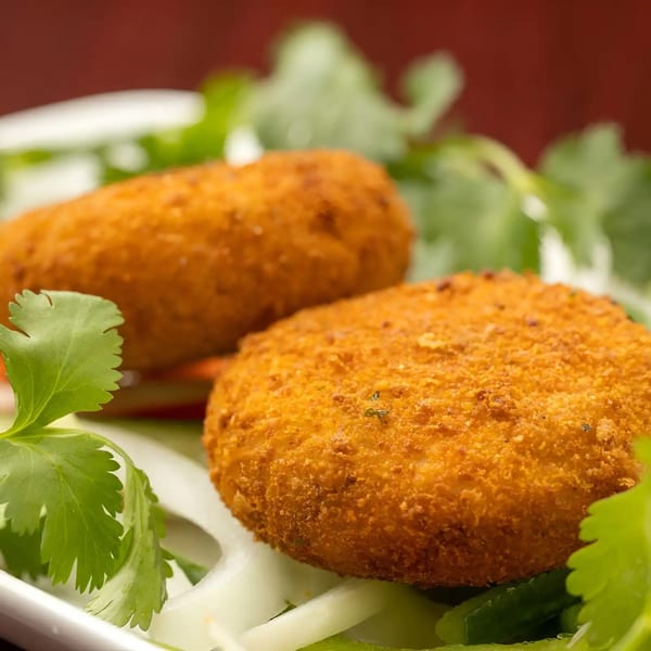 Two golden-brown fried croquettes sit on a bed of sliced onions and fresh cilantro.