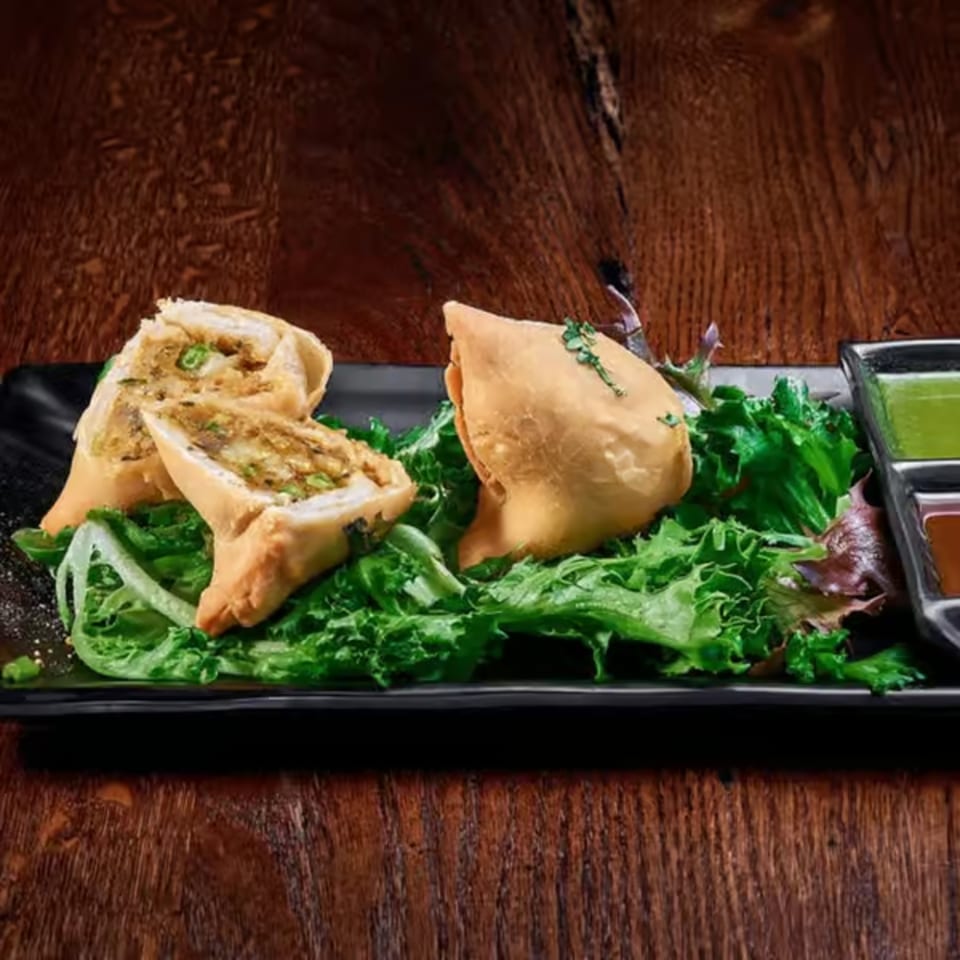 Crispy samosas, one cut open, served on a bed of lettuce with two dipping sauces.
