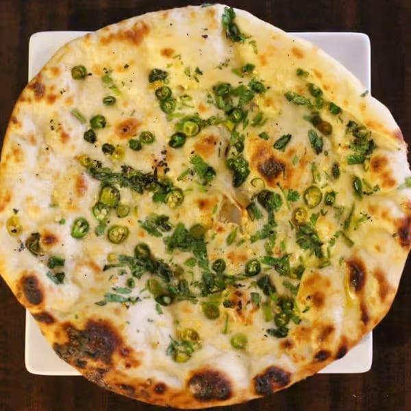 Close-up of a round naan bread topped with green chilies and cilantro on a white plate.