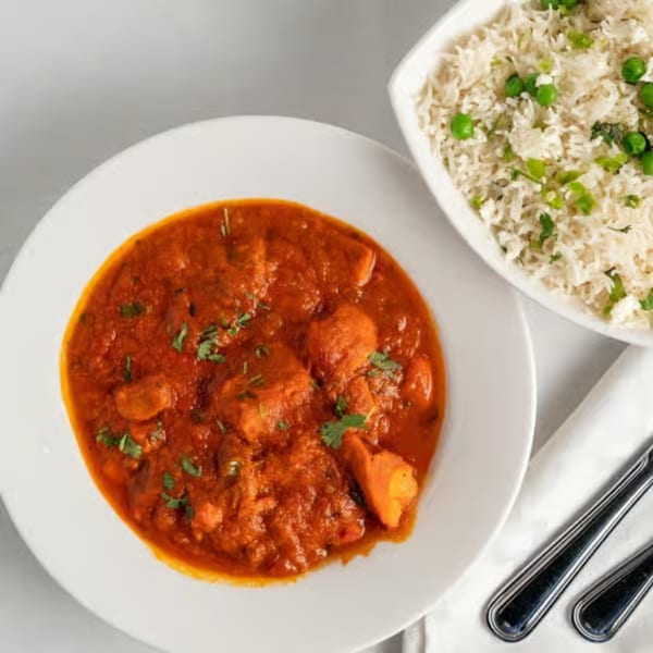 A bowl of chicken tikka masala with cilantro, next to a bowl of rice with peas and herbs.
