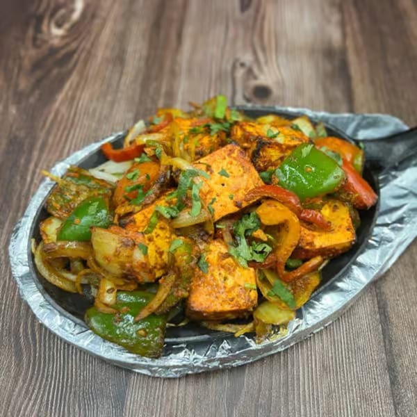 Sizzling paneer fajitas with colorful bell peppers and onions on a dark wooden table.