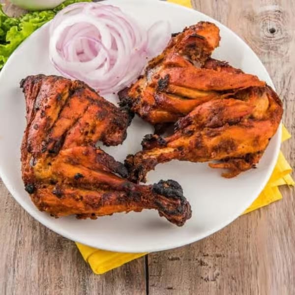 Three pieces of tandoori chicken with sliced red onions on a white plate.