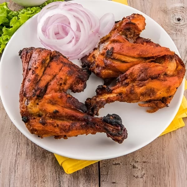 Three pieces of grilled tandoori chicken with sliced red onions and lettuce on a white plate.