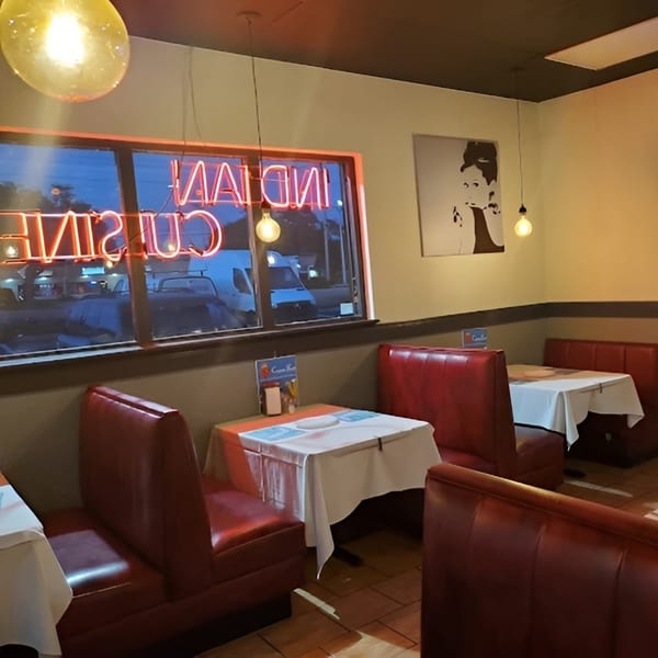Interior of an Indian restaurant with red booths, white tablecloths, and a neon "Indian Cuisine" sign.