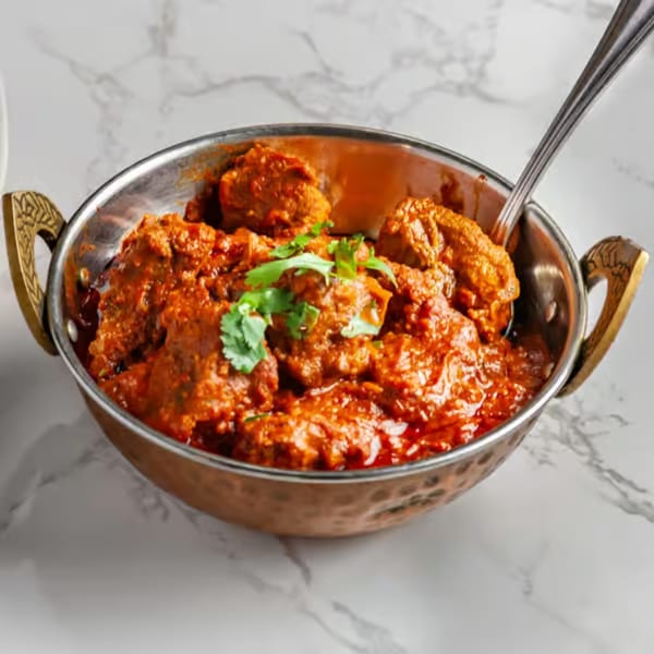 A copper karahi bowl filled with rich red chicken curry, garnished with fresh cilantro.