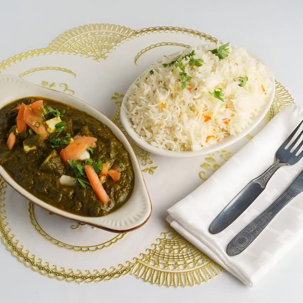 Palak paneer with tomatoes and cilantro, served with white rice and silverware on a white placemat.